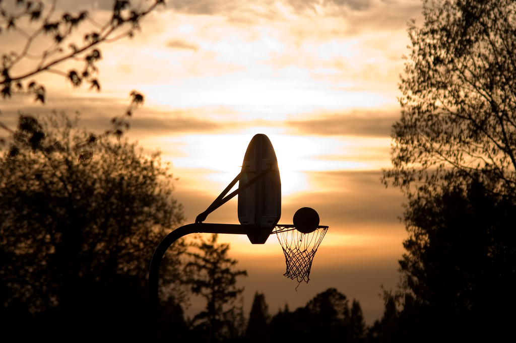 Image of a basketball going into a hoop with a sunset in the background